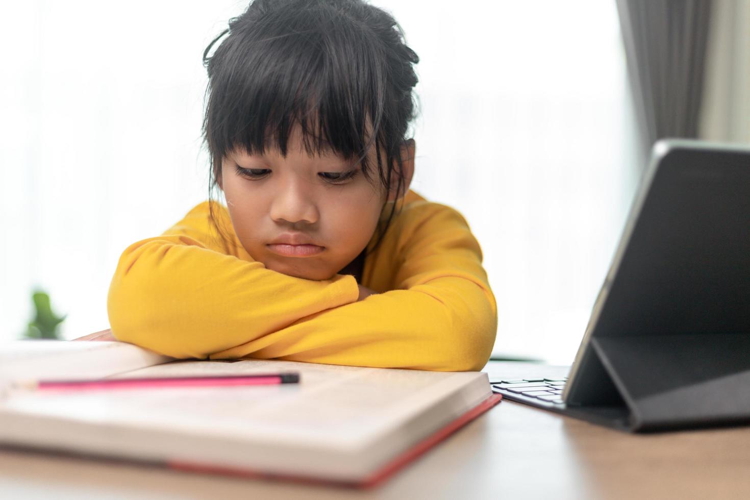 Little Asian girl sitting alone and looking out with a bored face, Preschool child laying head down on the table with sad  bored with homework, spoiled child photo