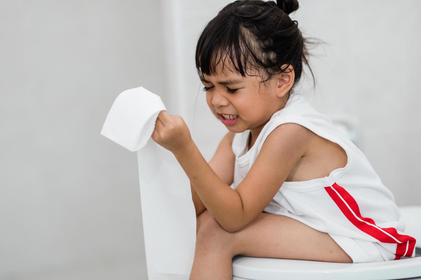 The little girl is sitting on the toilet suffering from constipation or hemorrhoid. photo