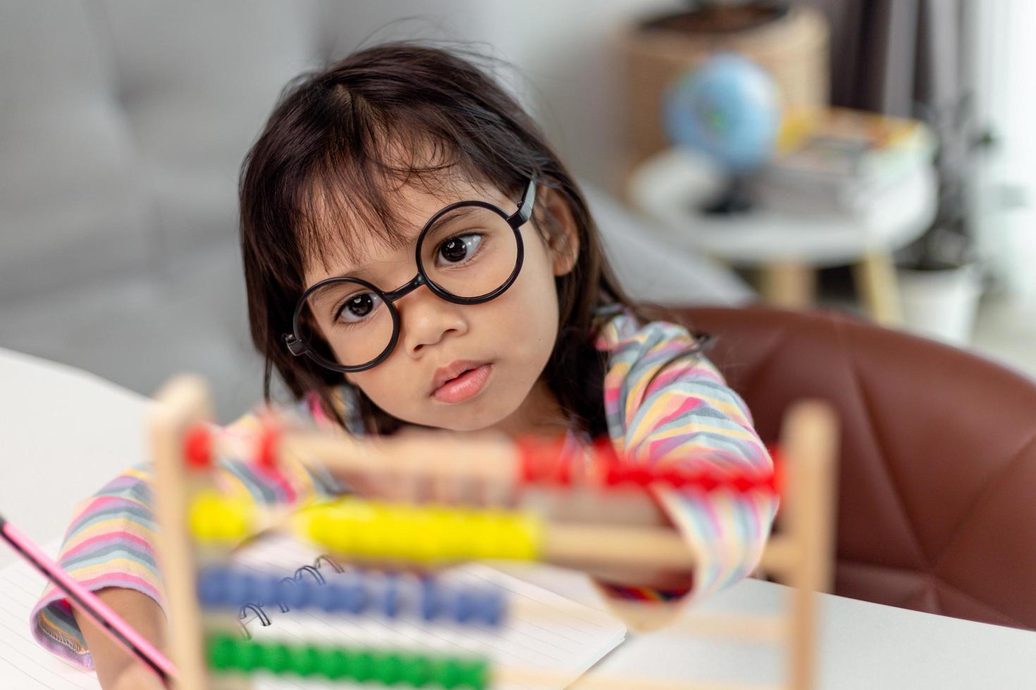 A young cute Asian girl is using the abacus with colored beads to learn how to count at home photo