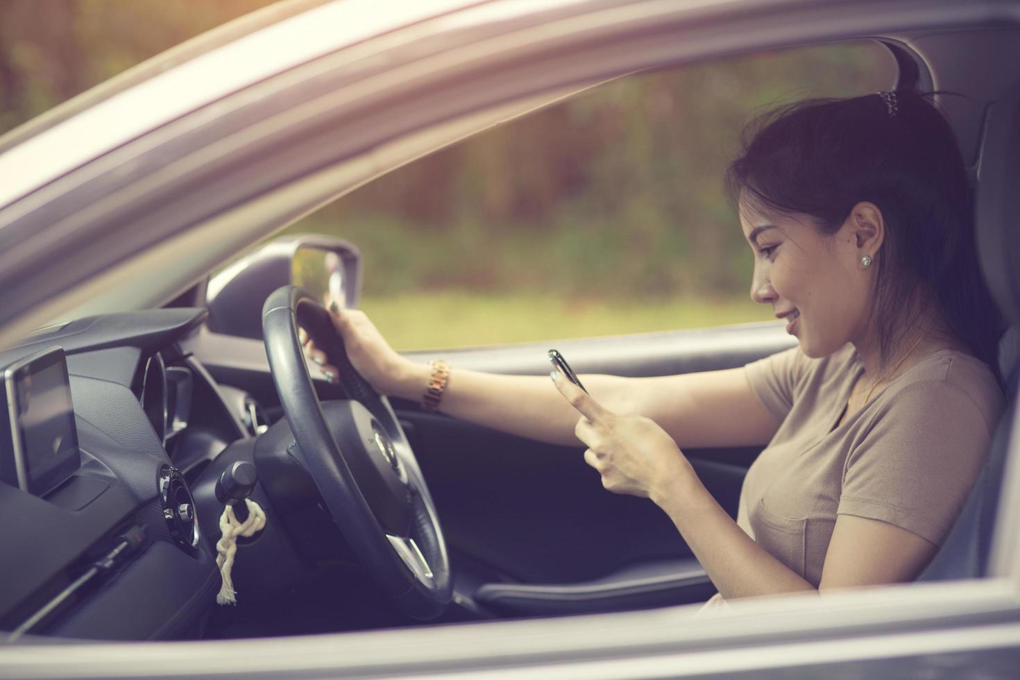 Young woman looking at her smartphone while driving a car on a sunny day with sun light coming through windshield photo