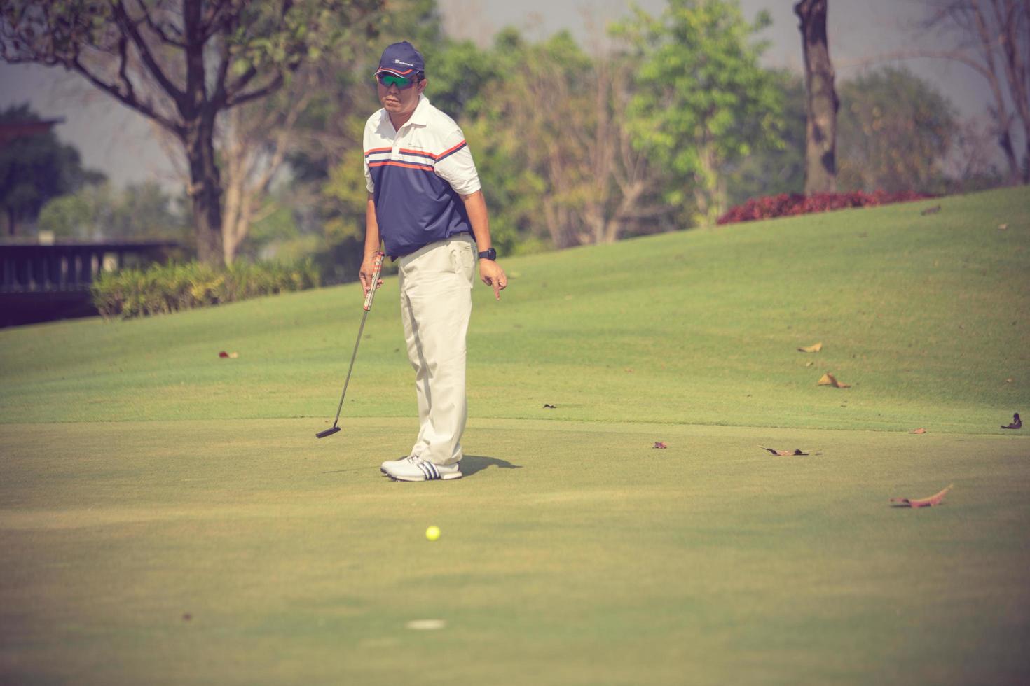 Golf player at the putting green hitting ball into a hole.Vintage color photo