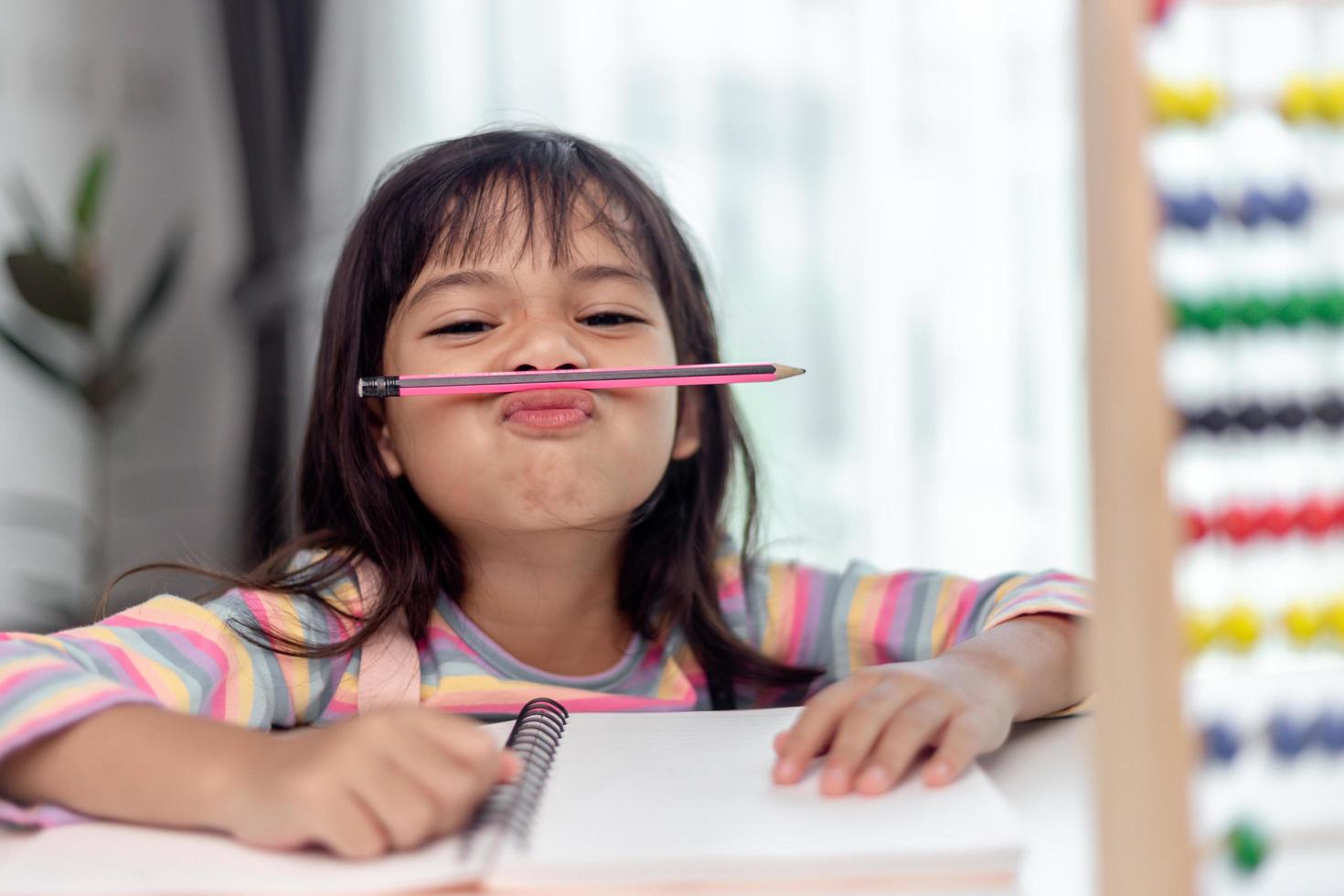 funny girl playing holding pen between nose and lips as mustache looking at the camera, playful bored after learning long hours. photo