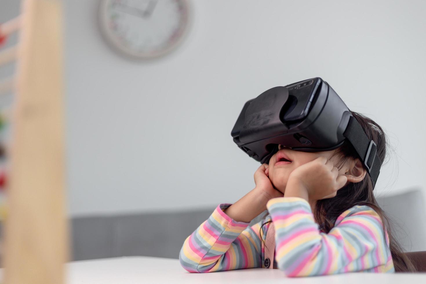 niño con casco de realidad virtual sentado detrás de la mesa en casa foto