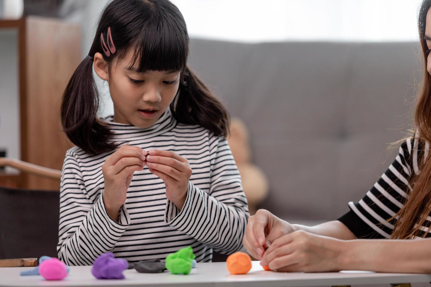 Asian mother and daughter play modeling clay together in kitchen with day light and they look happy. Concept of enjoy with family time photo