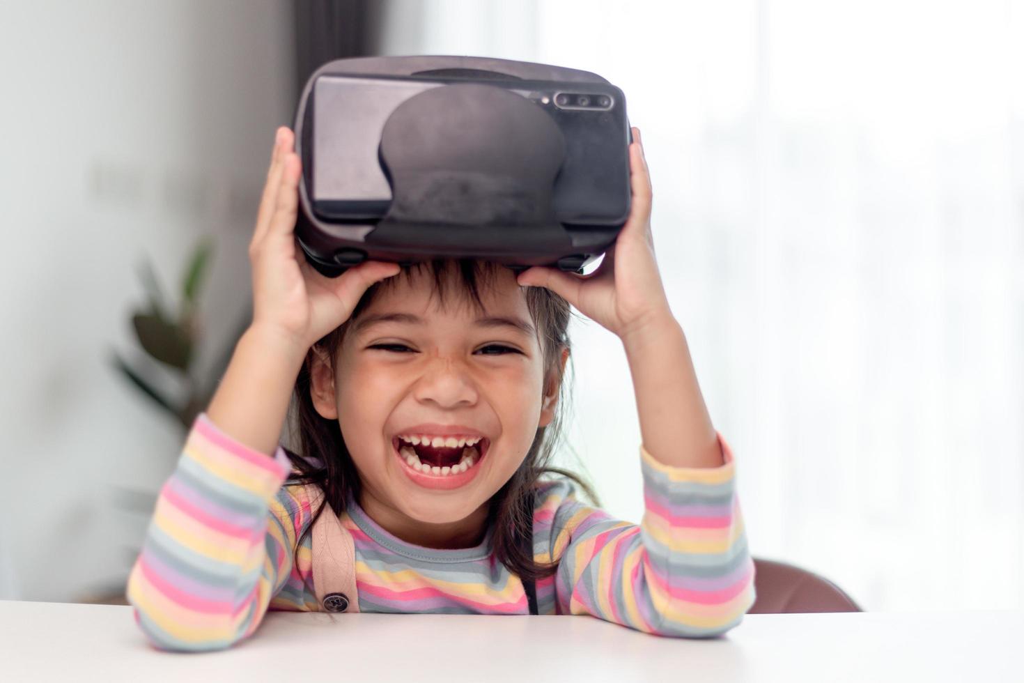 Child with virtual reality headset sitting behind table indoors at home photo