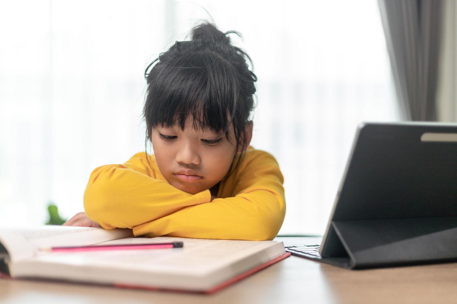 Little Asian girl sitting alone and looking out with a bored face, Preschool child laying head down on the table with sad  bored with homework, spoiled child photo