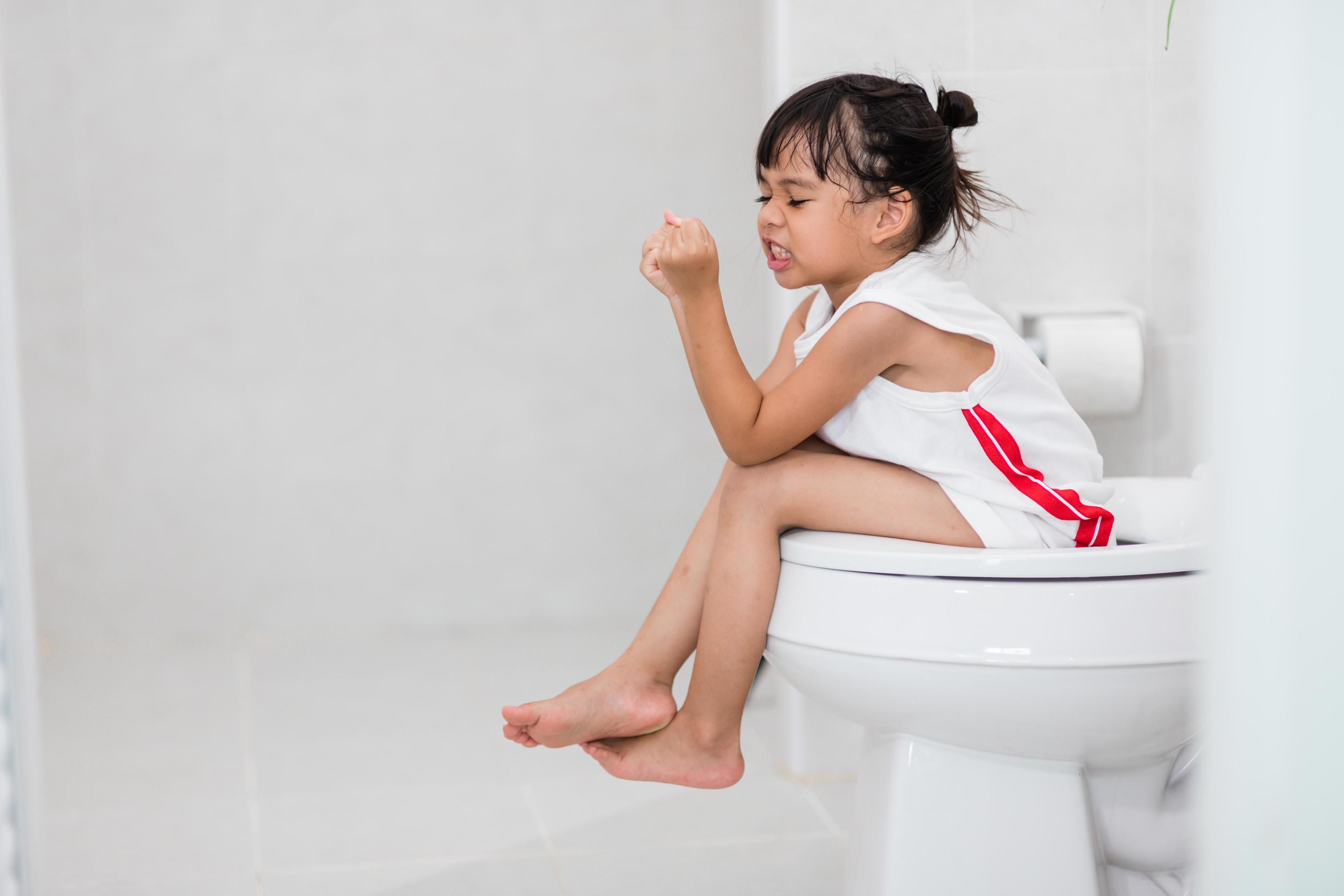 The little girl is sitting on the toilet suffering from constipation or