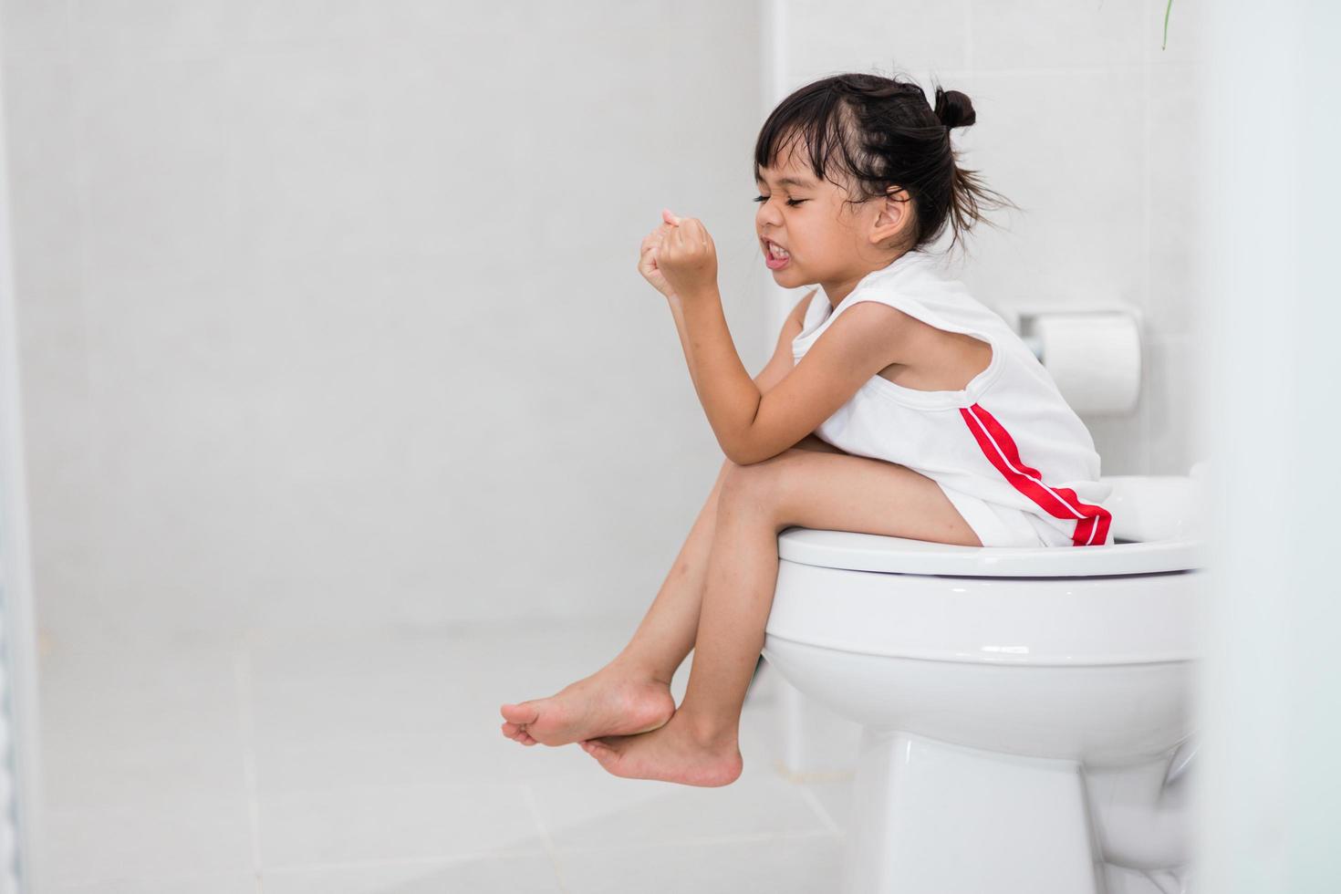 The little girl is sitting on the toilet suffering from constipation or hemorrhoid. photo