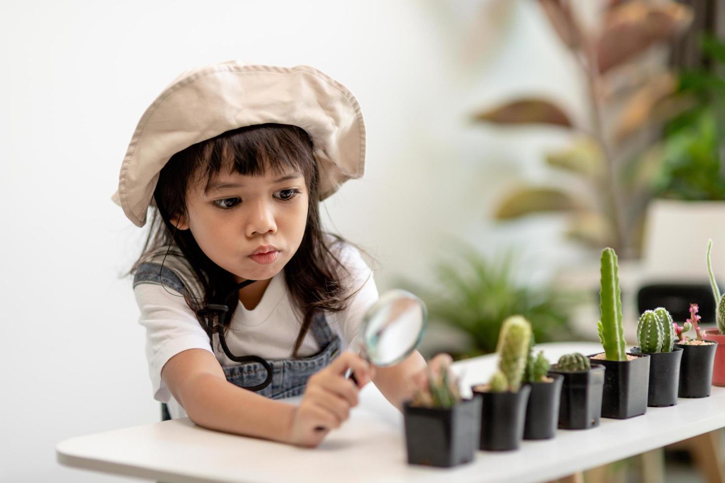 kid gently touch new stem of the cactus he grows with care, one hand holds magnifying glass.Nature education, Montessori and observation skills concept. photo