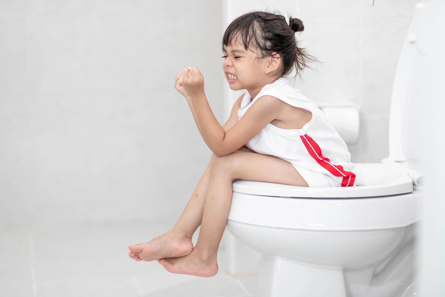 The little girl is sitting on the toilet suffering from constipation or hemorrhoid. photo