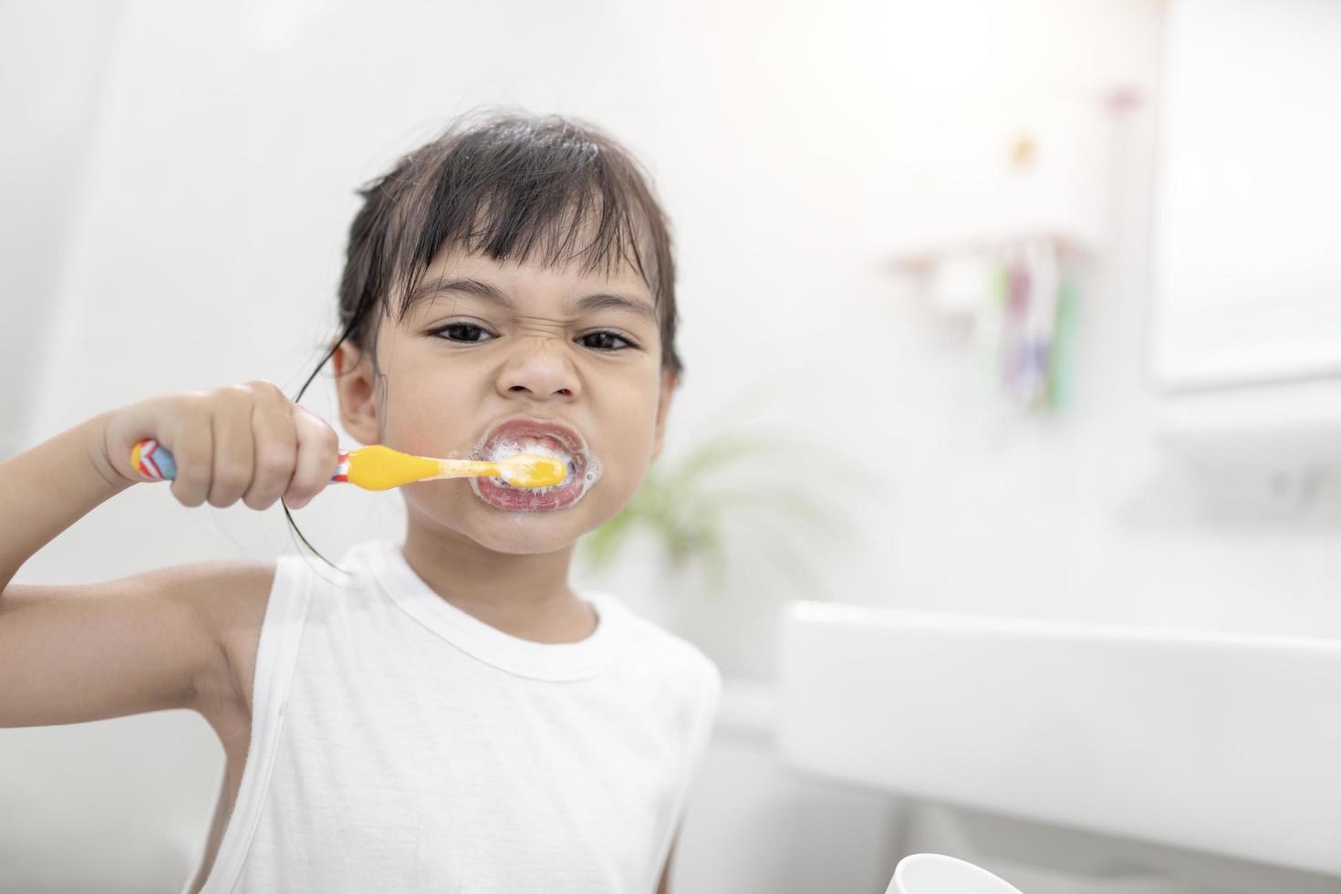 Little cute baby girl cleaning her teeth with a toothbrush in the bathroom photo