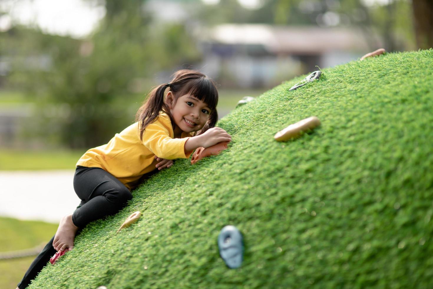 Cute Asian girl having fun trying to climb on artificial boulders at schoolyard playground, Little girl climbing up the rock wall, Hand Eye Coordination, Skills development photo