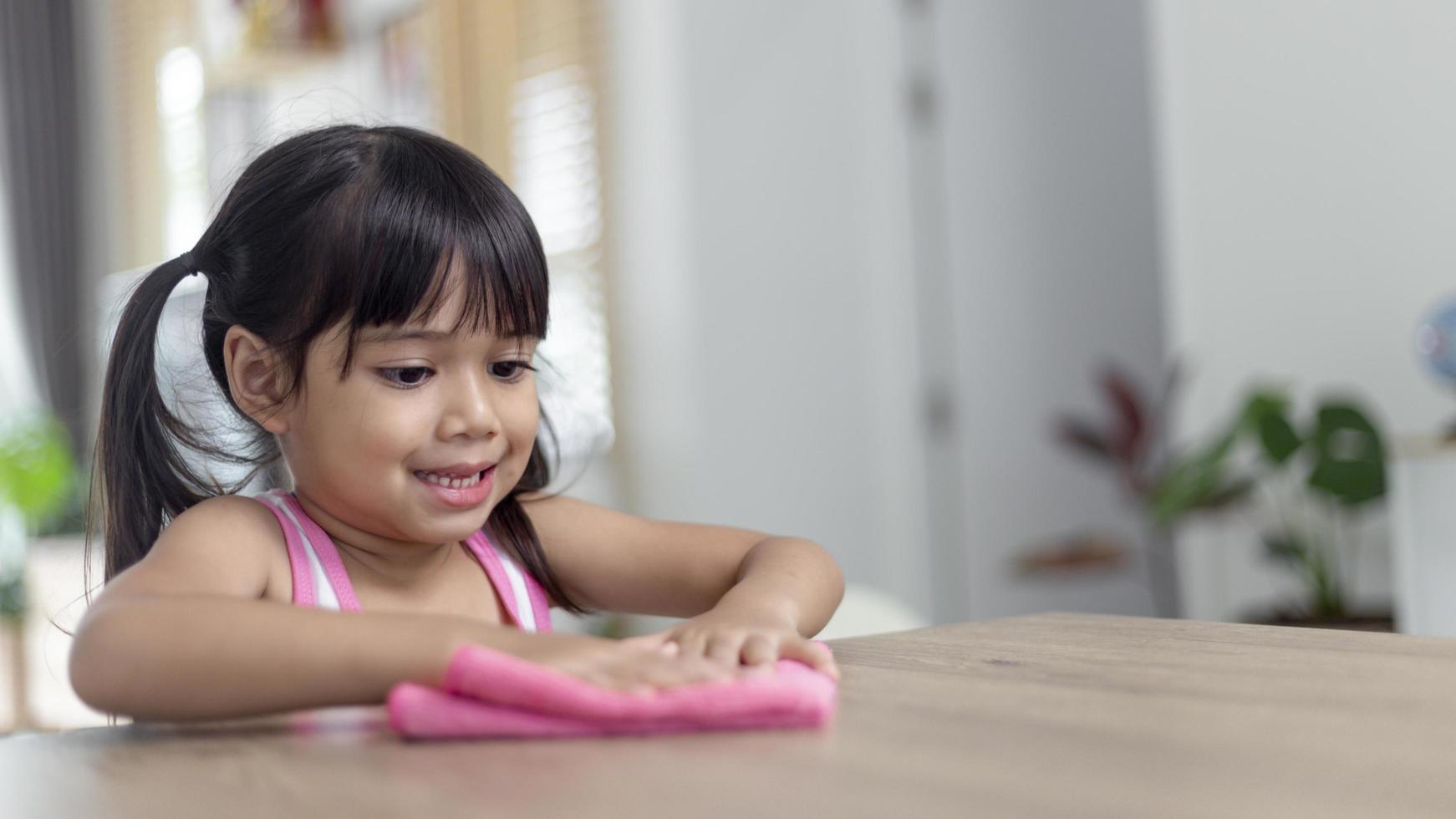 happy little Asian girl learning to clean with a rag in the living room at home. housework and household concept. photo