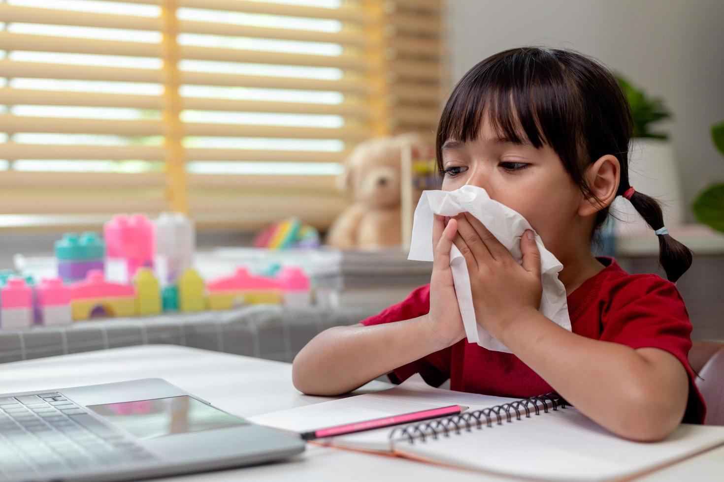 Unhealthy kid blowing nose into tissue, Child suffering from running nose or sneezing, A girl catches a cold when season change, childhood wiping nose with tissue photo