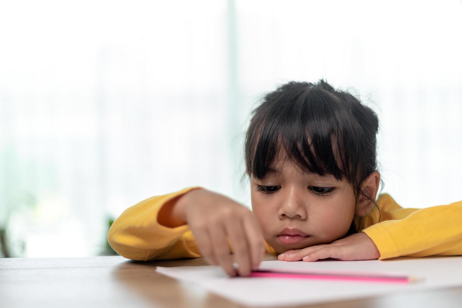 Little Asian girl sitting alone and looking out with a bored face, Preschool child laying head down on the table with sad  bored with homework, spoiled child photo