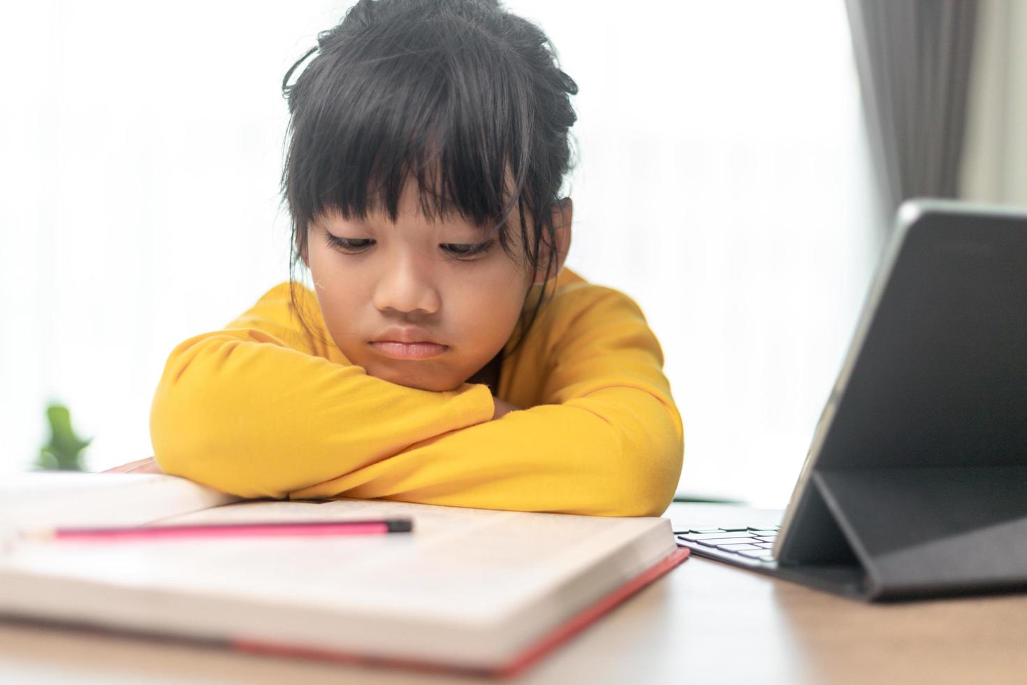 Little Asian girl sitting alone and looking out with a bored face, Preschool child laying head down on the table with sad  bored with homework, spoiled child photo