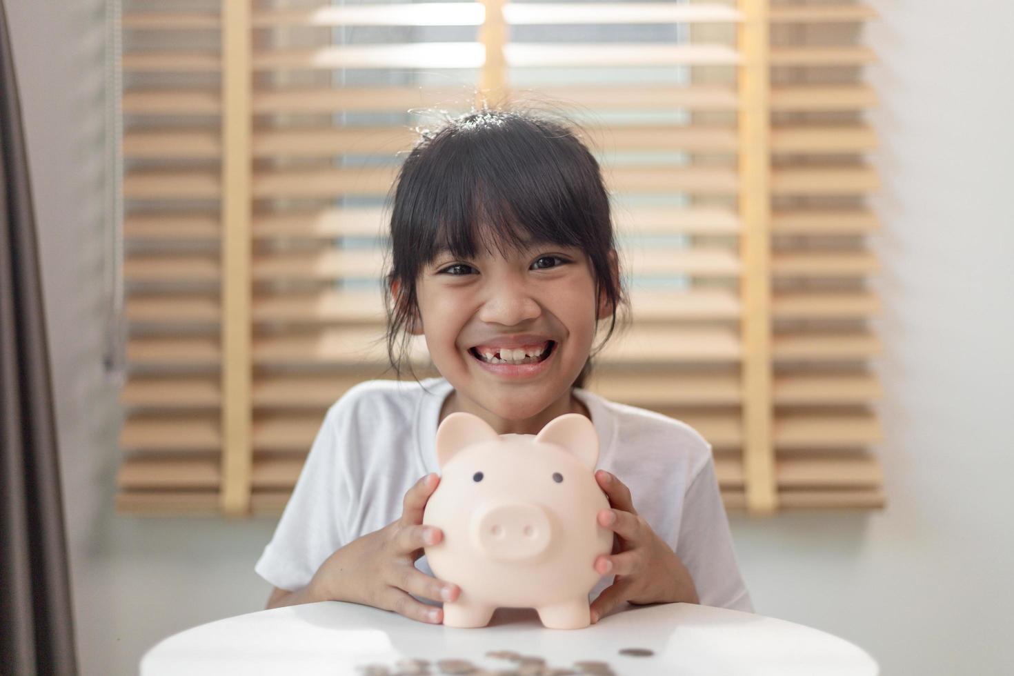 Little Asian girl saving money in a piggy bank, learning about saving, Kid save money for future education. Money, finances, insurance, and people concept photo