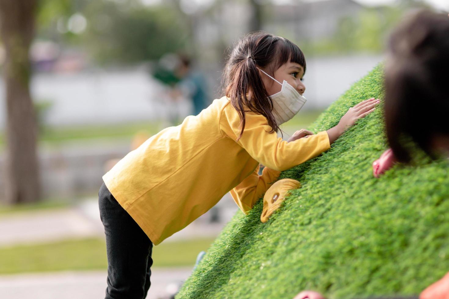 Cute Asian girl having fun trying to climb on artificial boulders at schoolyard playground, Little girl climbing up the rock wall, Hand Eye Coordination, Skills development photo