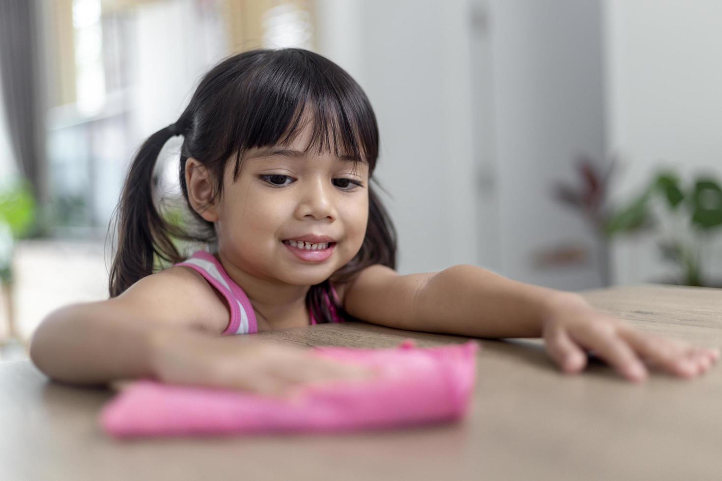 niña asiática feliz aprendiendo a limpiar con un trapo en la sala de estar en casa. tareas domésticas y concepto de hogar. foto