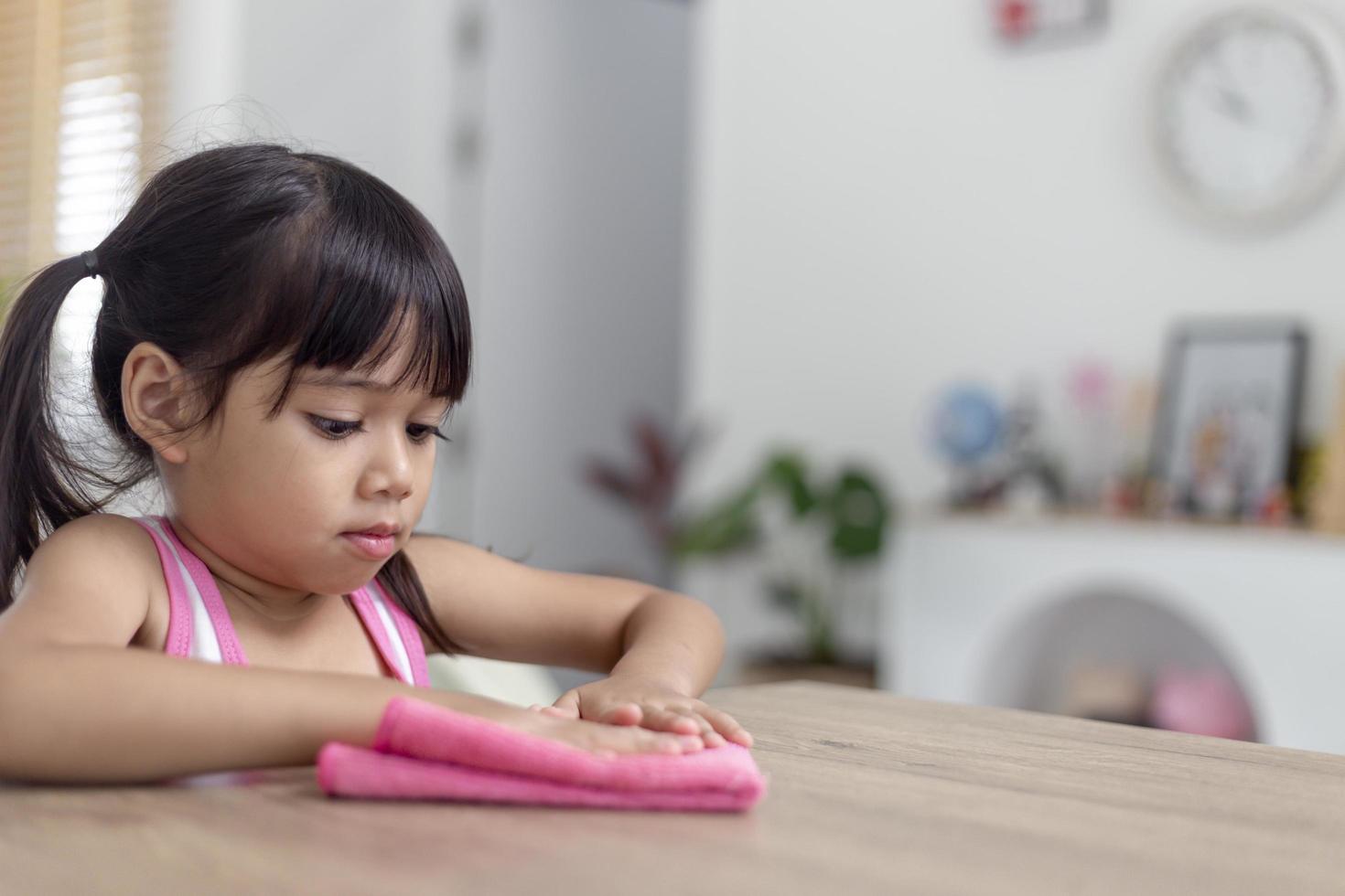 niña asiática feliz aprendiendo a limpiar con un trapo en la sala de estar en casa. tareas domésticas y concepto de hogar. foto