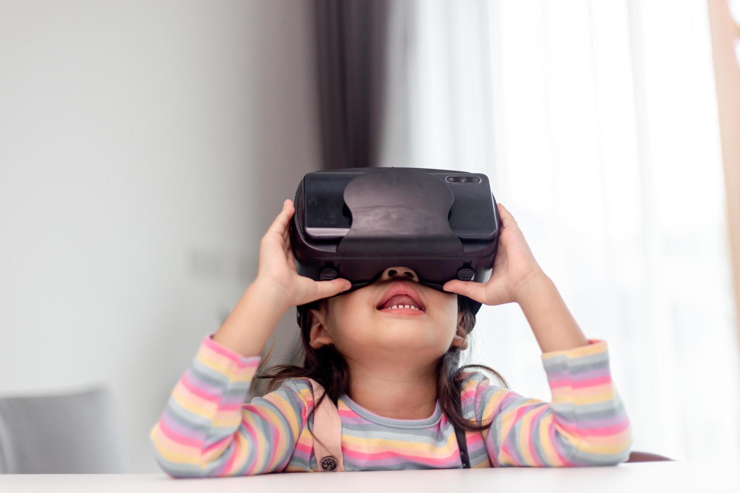 niño con casco de realidad virtual sentado detrás de la mesa en casa foto