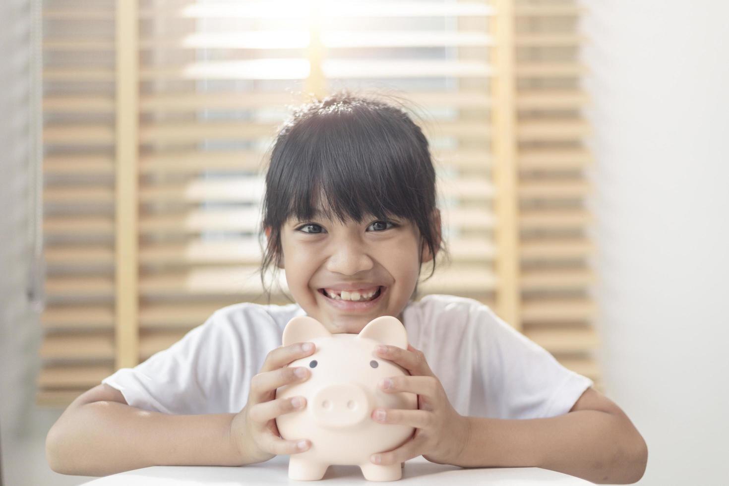 niña asiática ahorrando dinero en una alcancía, aprendiendo a ahorrar, los niños ahorran dinero para la educación futura. concepto de dinero, finanzas, seguros y personas foto