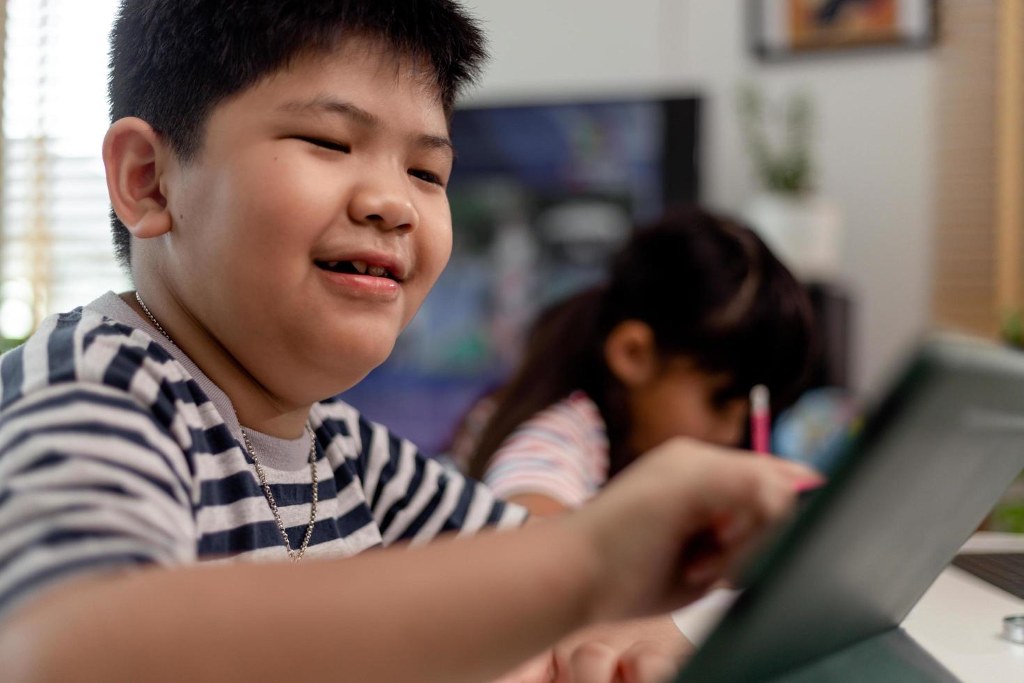 Asian boys and girls enjoy online learning by taking notes and using tablets at home. photo