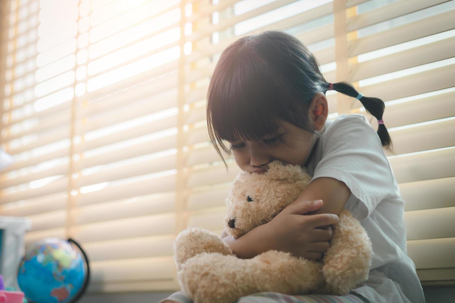 Close up lonely little girl hugging toy, sitting at home alone, upset unhappy child waiting for parents, thinking about problems, bad relationship in family, psychological trauma photo