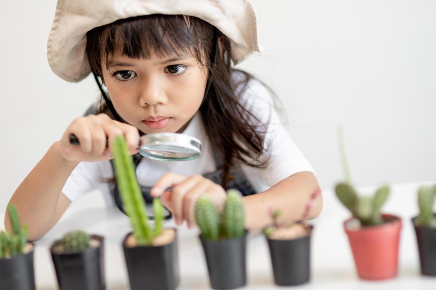 kid gently touch new stem of the cactus he grows with care, one hand holds magnifying glass.Nature education, Montessori and observation skills concept. photo