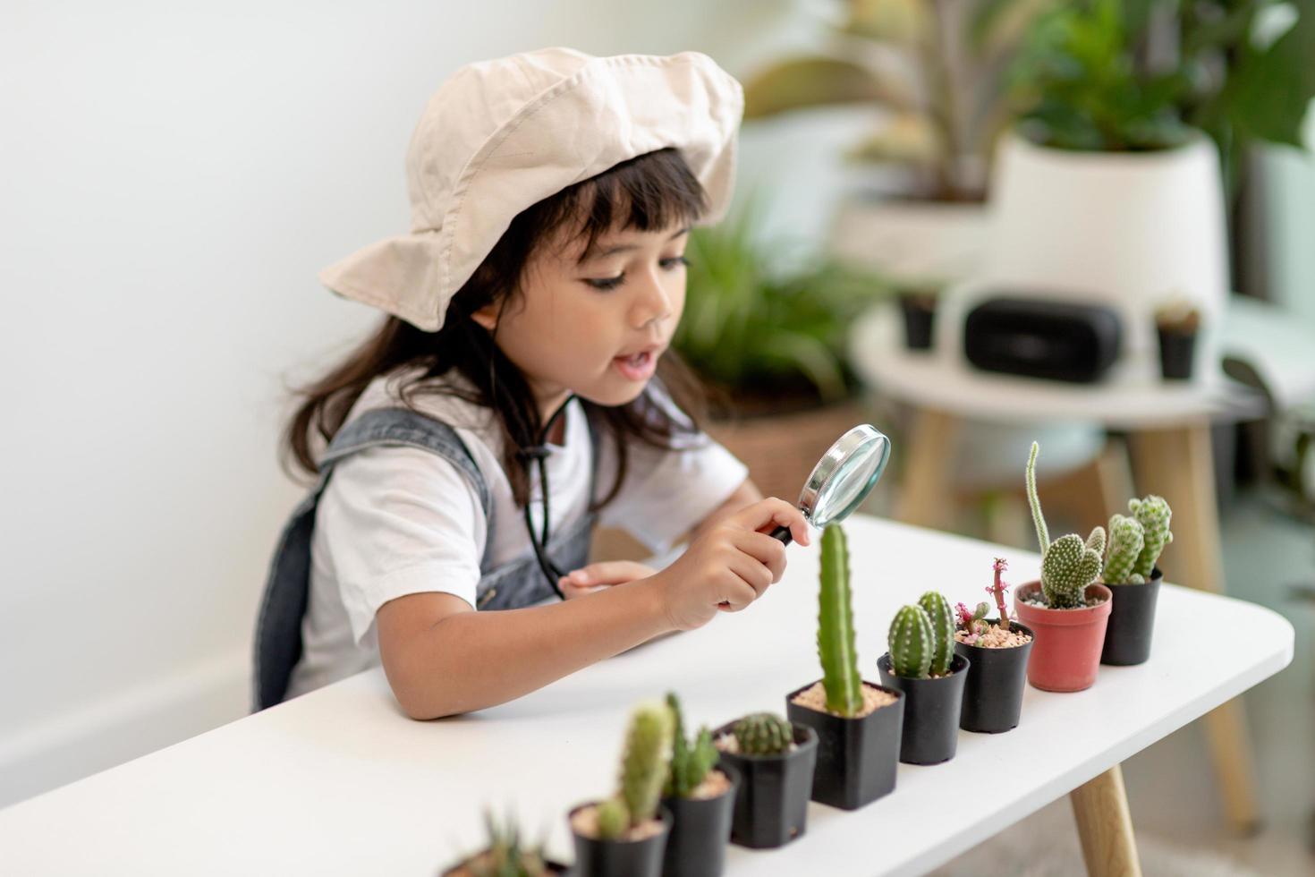 kid gently touch new stem of the cactus he grows with care, one hand holds magnifying glass.Nature education, Montessori and observation skills concept. photo