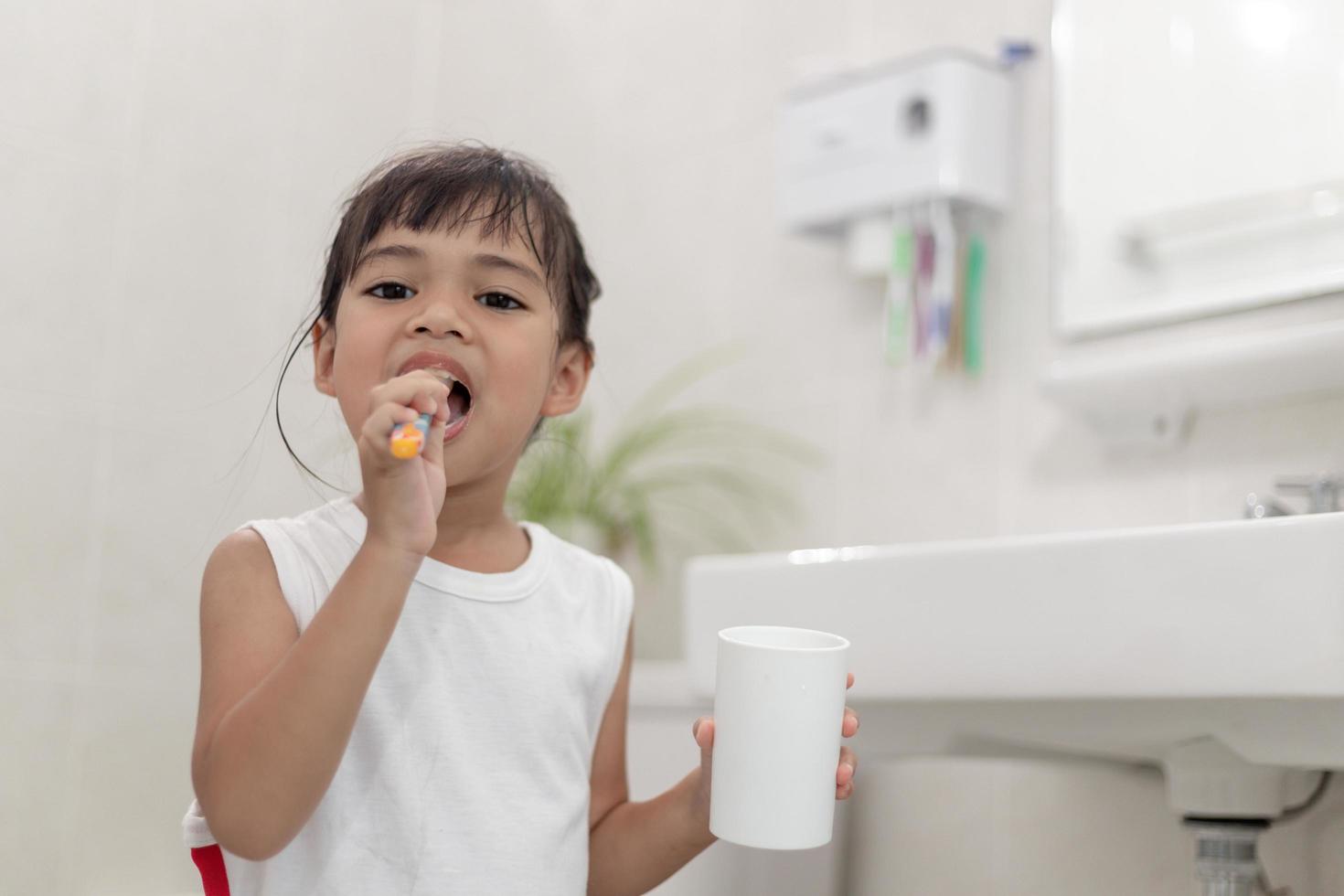 pequeña y linda niña limpiándose los dientes con un cepillo de dientes en el baño foto