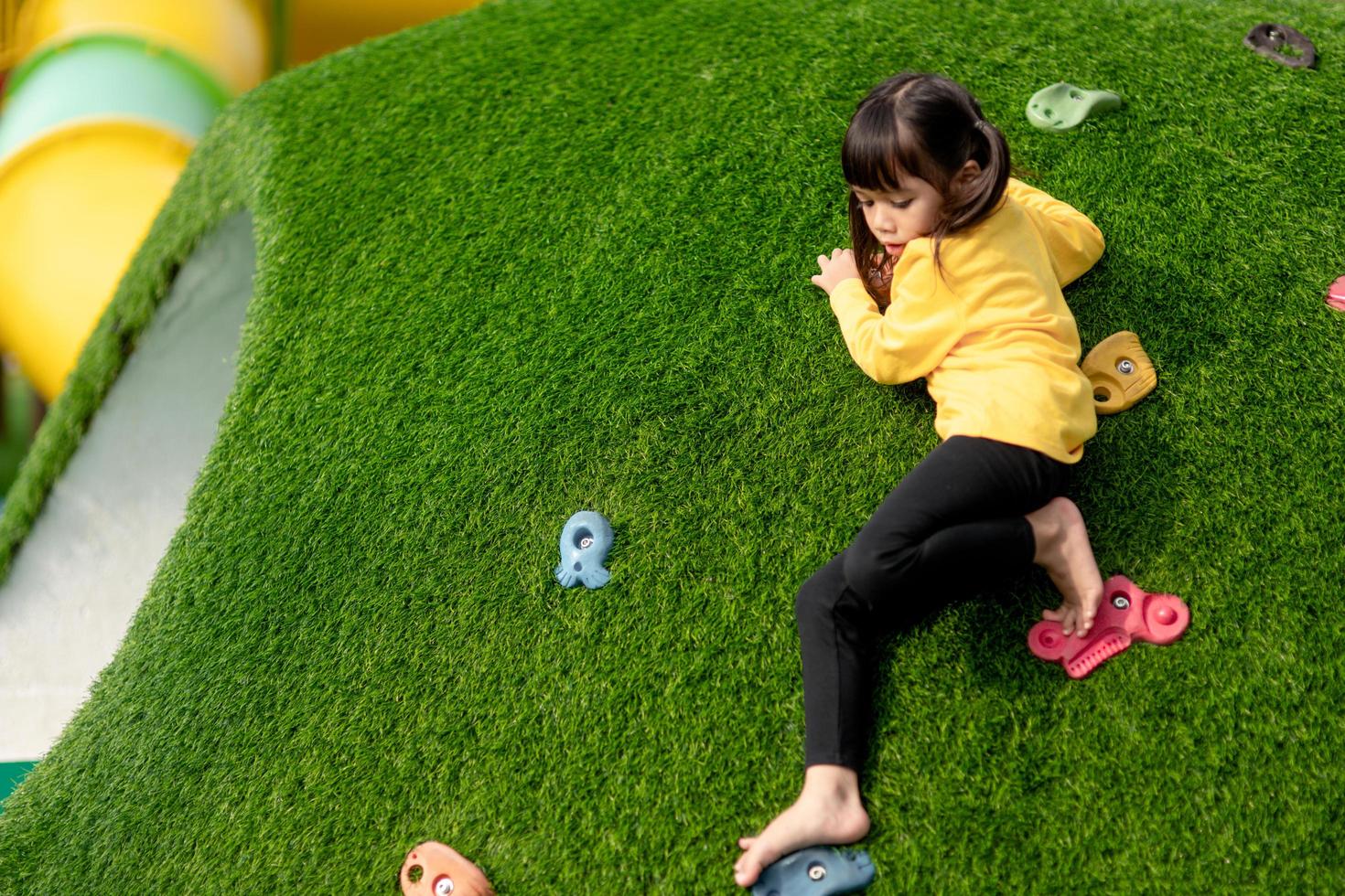 Cute Asian girl having fun trying to climb on artificial boulders at schoolyard playground, Little girl climbing up the rock wall, Hand Eye Coordination, Skills development photo