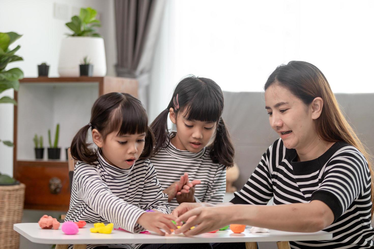 Asian mother and daughter play modeling clay together in kitchen with day light and they look happy. Concept of enjoy with family time photo