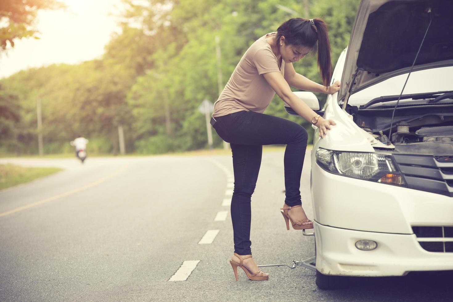 Young woman changing flat tire in field photo