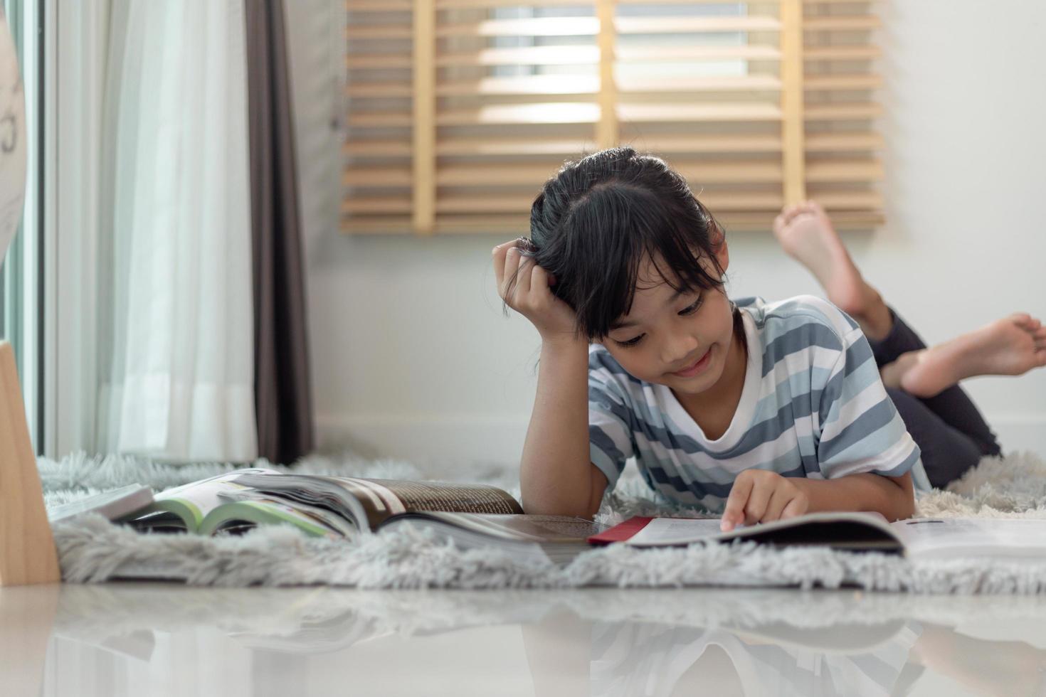 Child reading book at home. Girl lying and reading indoors photo