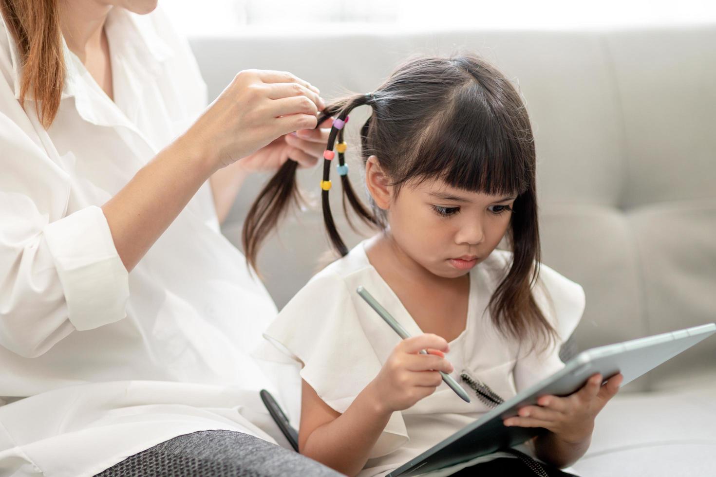 Young Asian mother tying daughter's hair photo