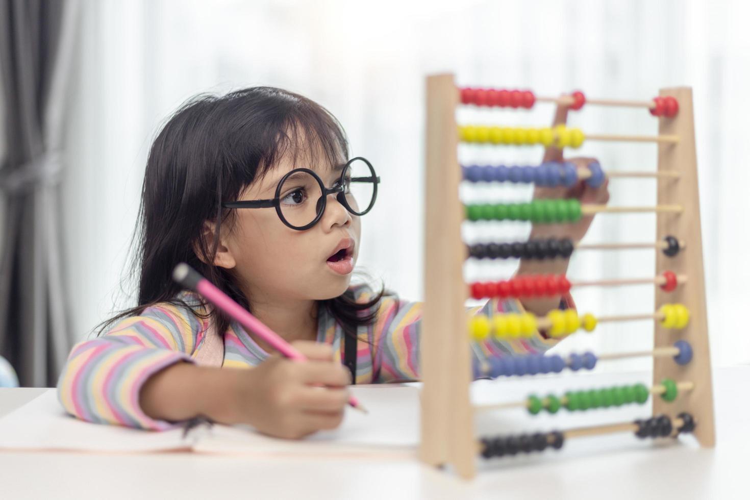 A young cute Asian girl is using the abacus with colored beads to learn how to count at home photo