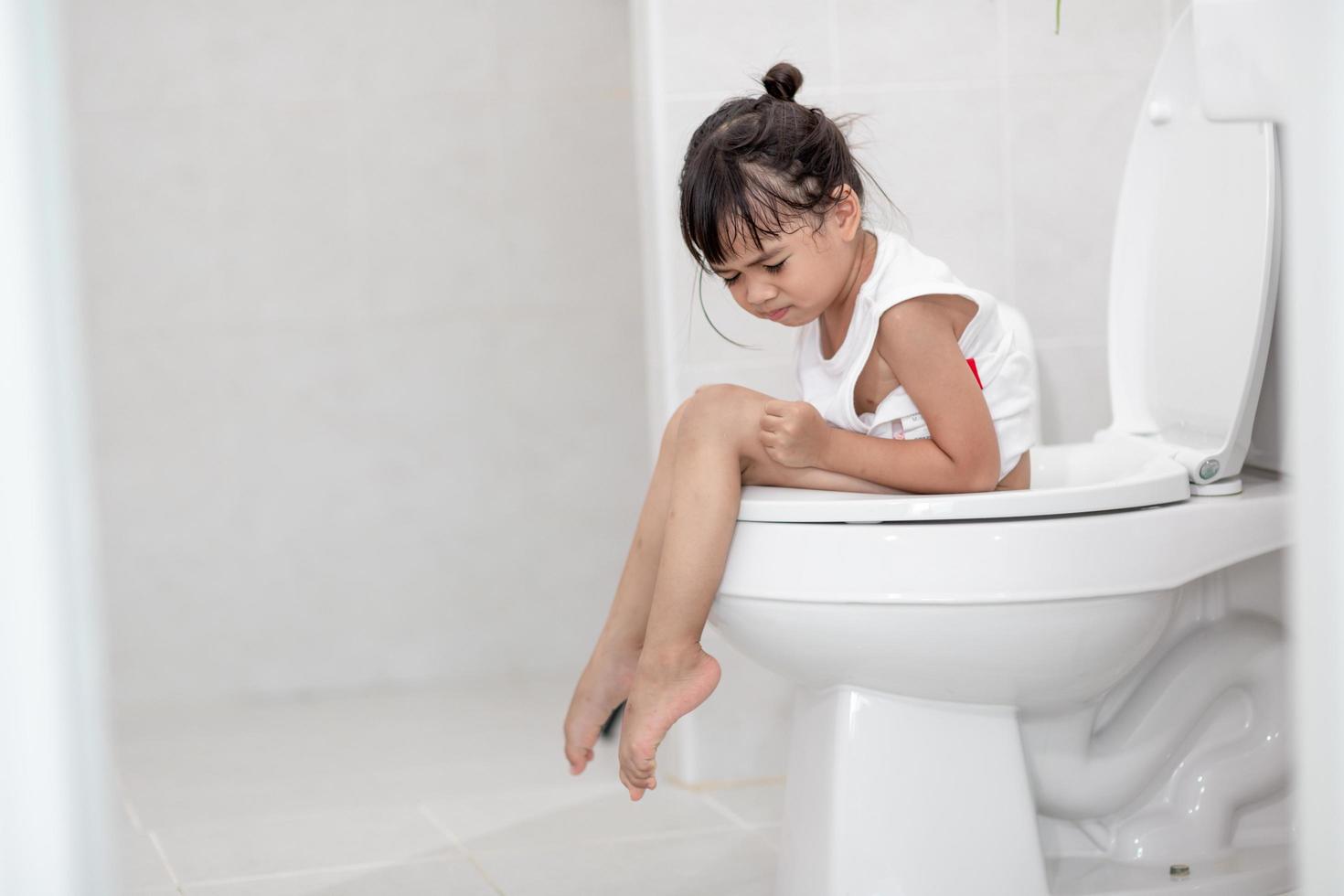 The little girl is sitting on the toilet suffering from constipation or hemorrhoid. photo