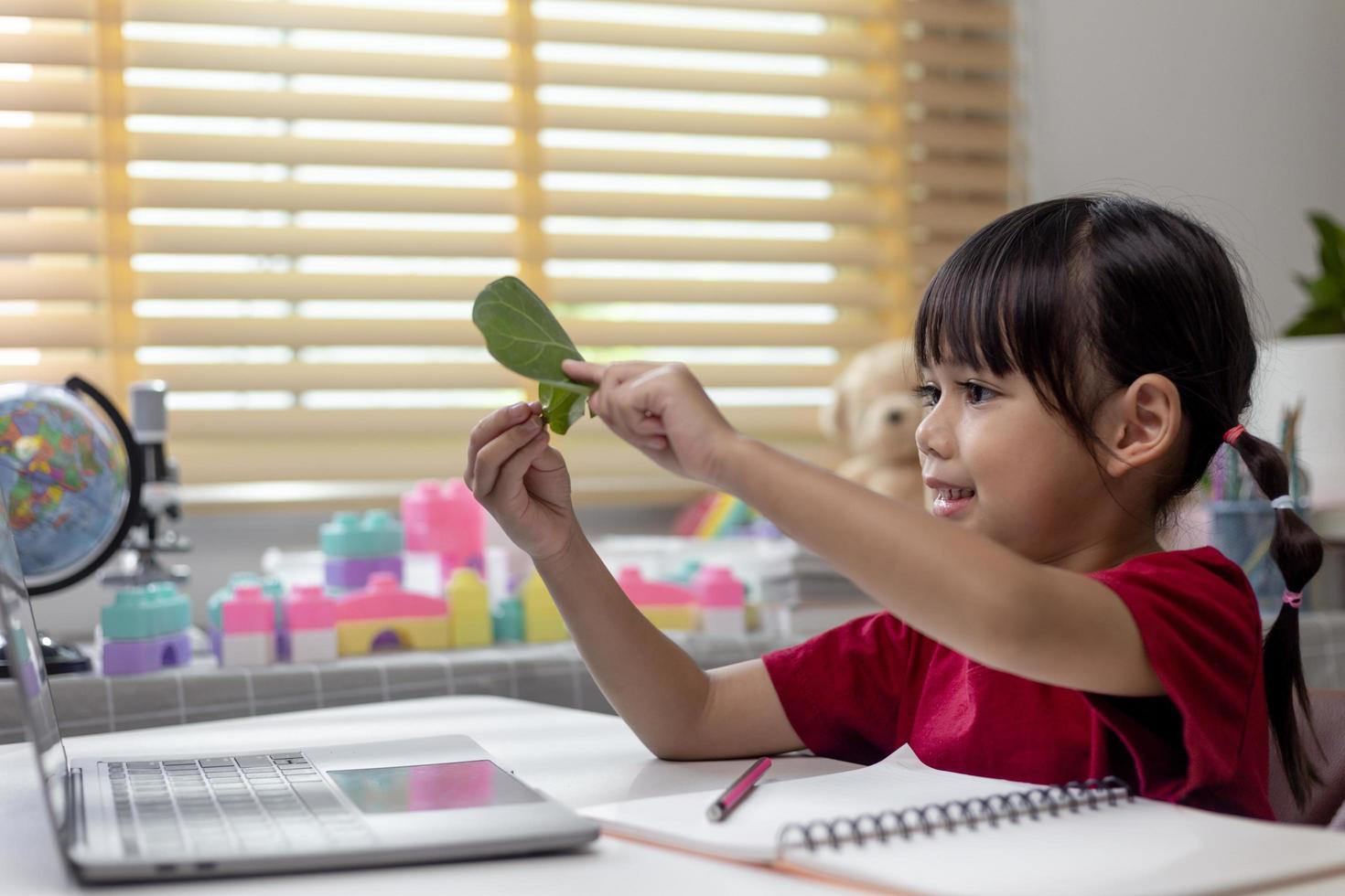 Learning time. Interested little kid schoolgirl in headset sit at home desk watch education video lesson. Curious small school age girl think on teacher question select correct answer on laptop screen photo