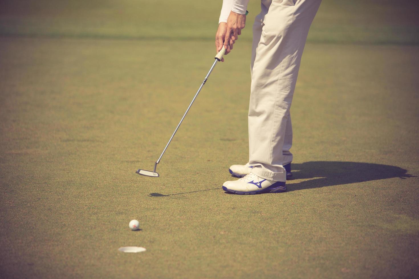 Golf player at the putting green hitting ball into a hole.Vintage color photo