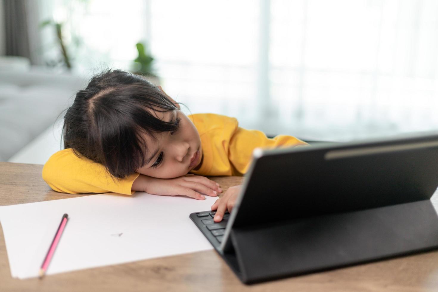 Little Asian girl sitting alone and looking out with a bored face, Preschool child laying head down on the table with sad  bored with homework, spoiled child photo