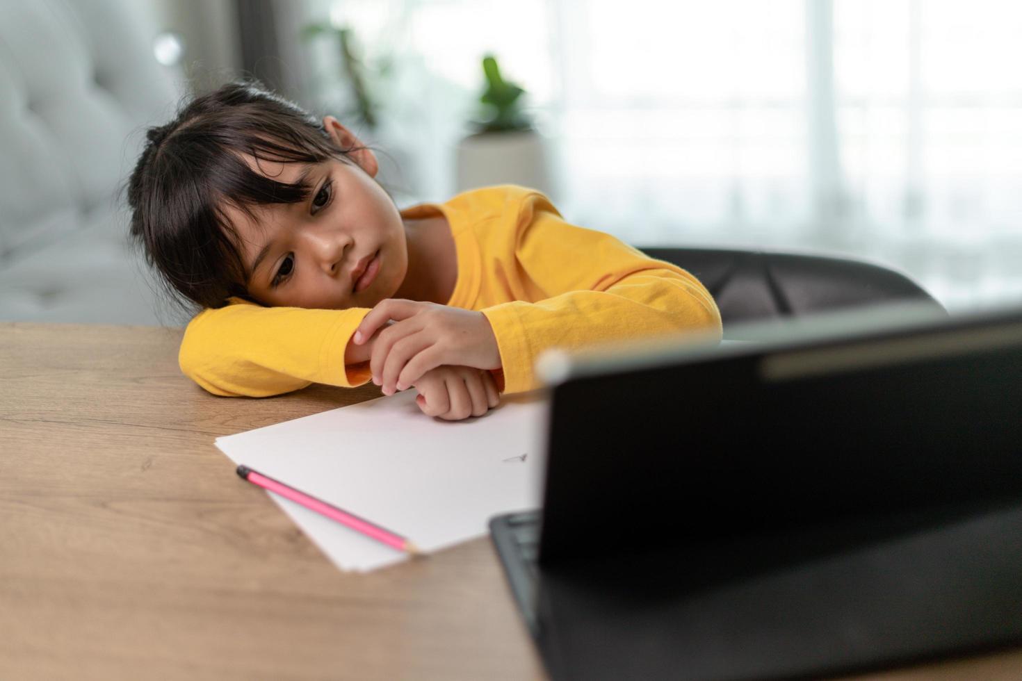 Little Asian girl sitting alone and looking out with a bored face, Preschool child laying head down on the table with sad  bored with homework, spoiled child photo