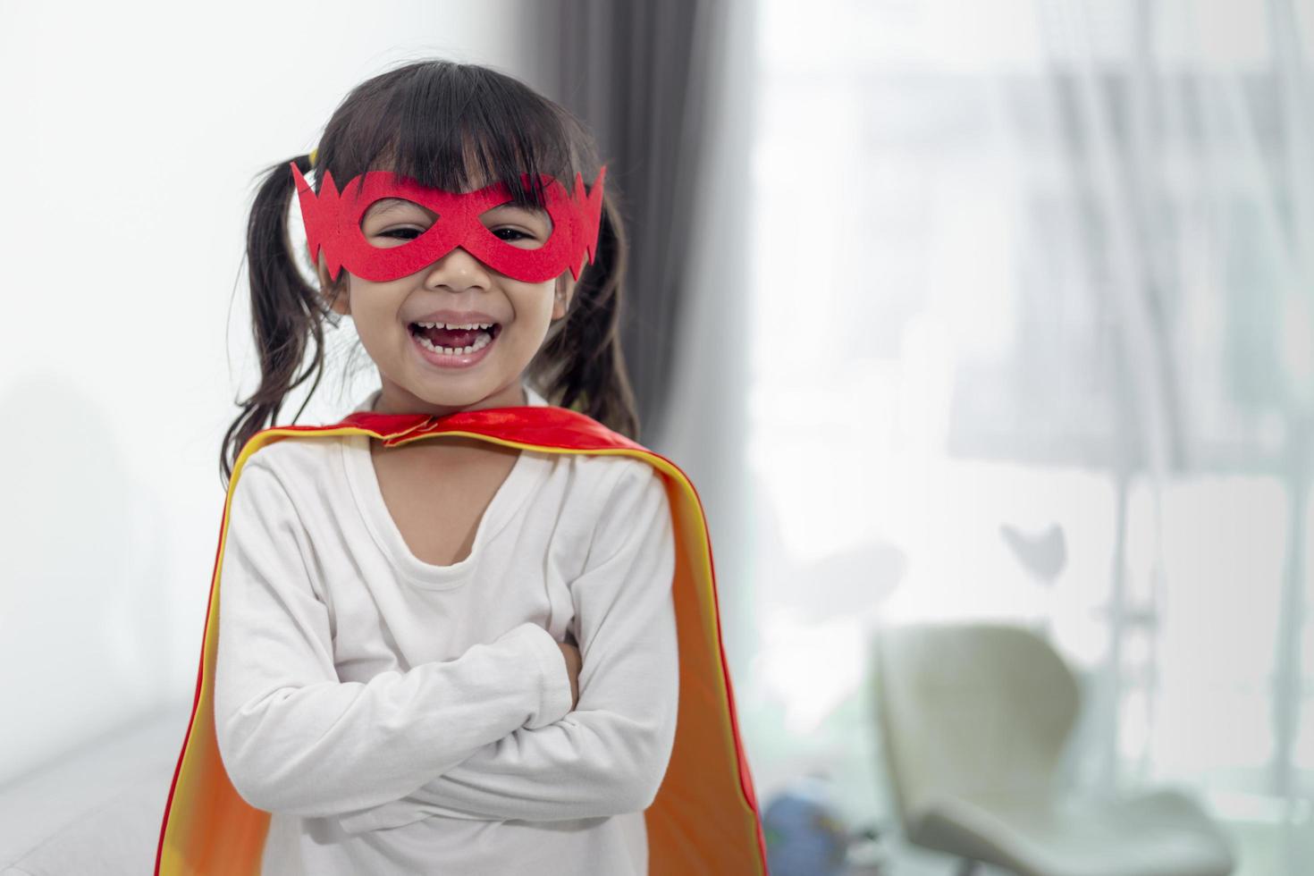 niña disfrazada de superhéroe con máscara y capa roja en casa foto