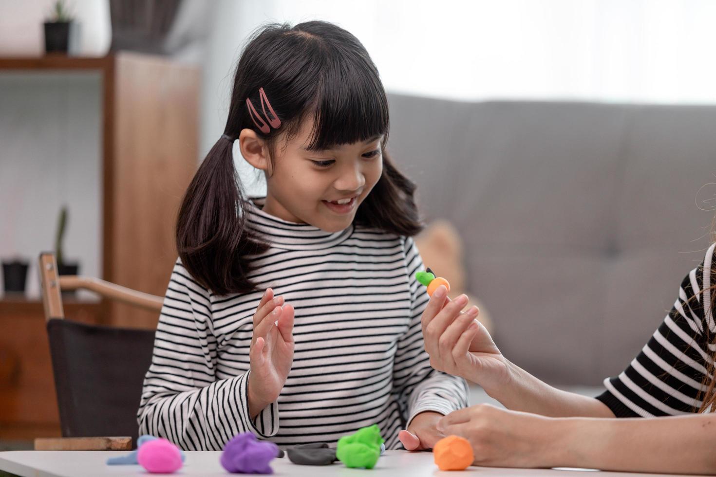 Asian mother and daughter play modeling clay together in kitchen with day light and they look happy. Concept of enjoy with family time photo