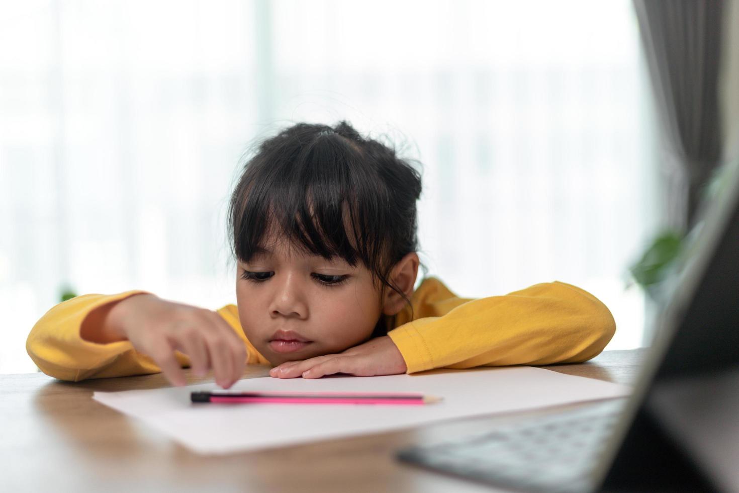 Little Asian girl sitting alone and looking out with a bored face, Preschool child laying head down on the table with sad  bored with homework, spoiled child photo