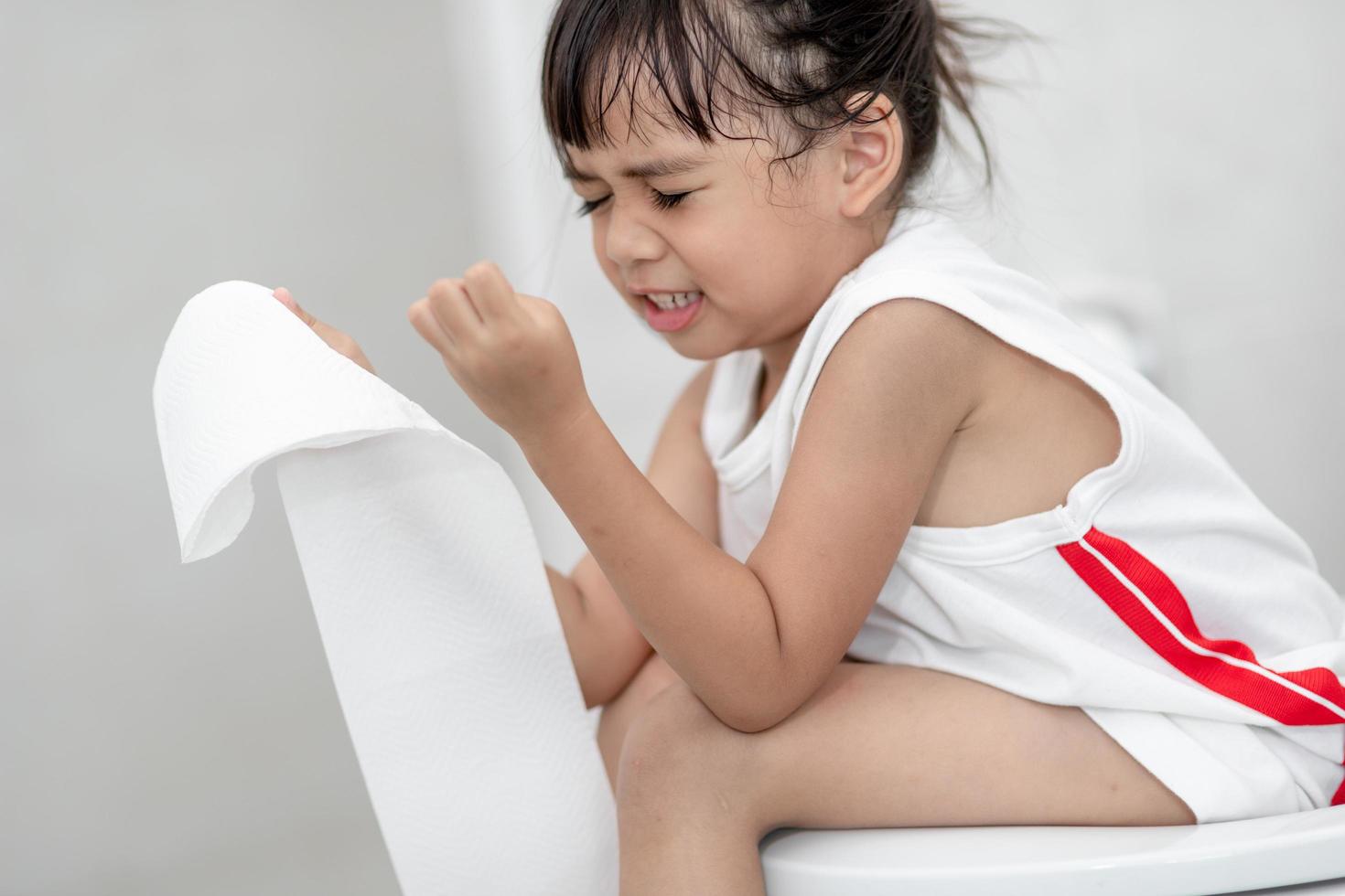 The little girl is sitting on the toilet suffering from constipation or hemorrhoid. photo