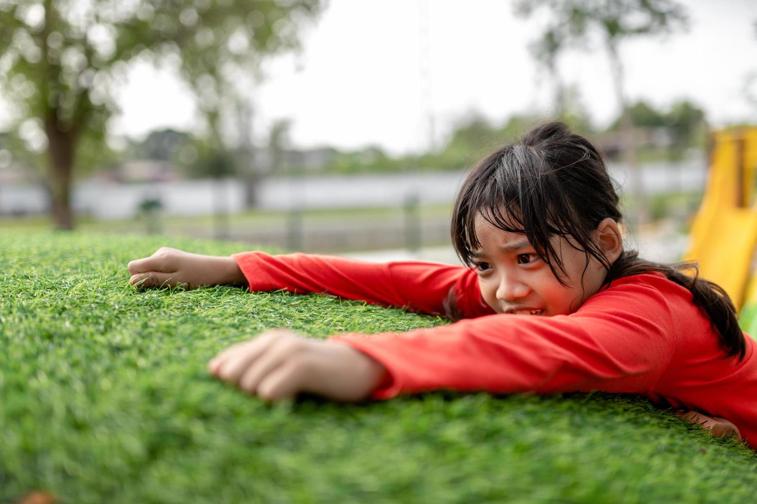 Cute Asian girl having fun trying to climb on artificial boulders at schoolyard playground, Little girl climbing up the rock wall, Hand Eye Coordination, Skills development photo