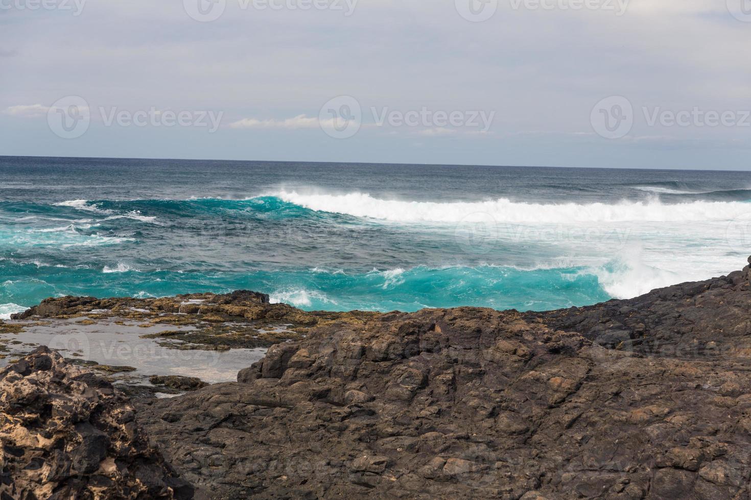 Turbulent ocean waves with white foam beat coastal stones photo