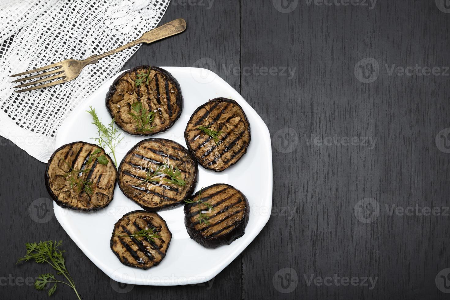 Grilled eggplants in plate on black wood background. photo