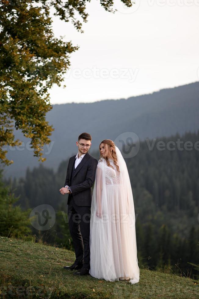 happy stylish bride and groom running and having fun in mountains on summer sunny day photo